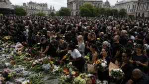 Large crowd gathered around floral tributes at a public vigil in a city square