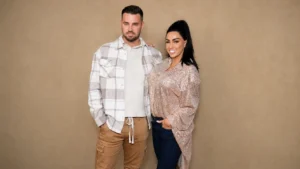Man and woman posing together against a beige studio background.