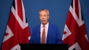Nigel Farage speaking at a podium between UK flags as the Clacton by-election result awaits official declaration