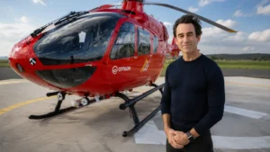 Red helicopter on a helipad with a man standing beside it