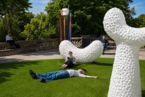 Visitors relaxing on a green lawn among large white sculptures and colourful outdoor artwork in a London sculpture garden