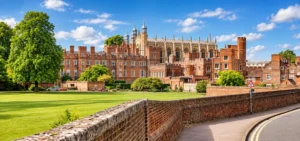 Wide view of a historic British independent school campus with red-brick buildings, manicured lawns and Gothic architecture under a bright blue sky