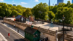 Wide view of an elevated London sculpture garden surrounded by trees, with colourful outdoor artworks and city buildings in the background.