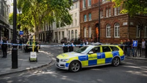 Wide view of police officers and a marked police car securing a city street junction with cordons in place during an emergency response.