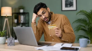 Worried man checking a bank card and laptop at home