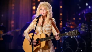 Dolly Parton performing on stage with an acoustic guitar during a live concert, representing the upcoming DollyFest London 2027 celebration